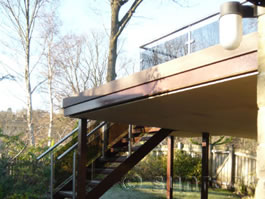 First floor balcony with tinted glass balustrades and steps built on top of a sealed extended deck area, creating an ideal rain-proof car-port